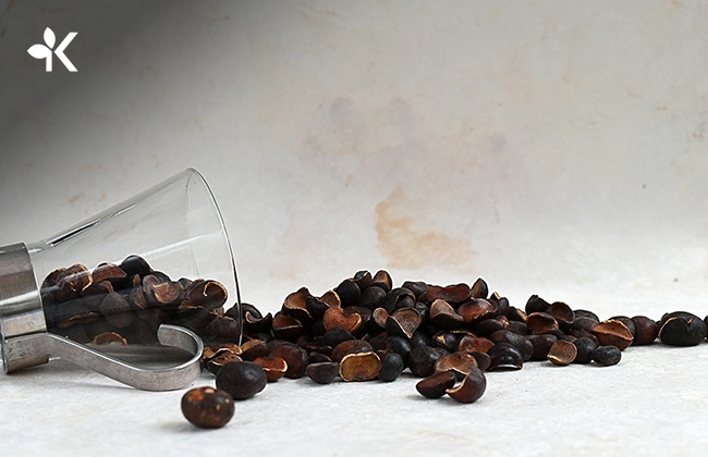 Taza de cristal volteada en una mesa y varias semillas de capomo saliendo de ella
