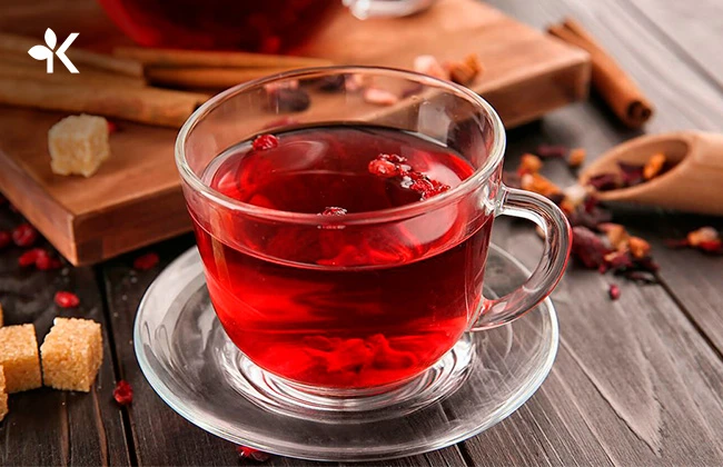 Taza de cristal con té de color rojo y algunos frutos en su interior