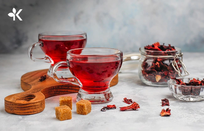 Dos tazas de té de color rojo, tres cubitos de azúcar y flores secas de hibisco